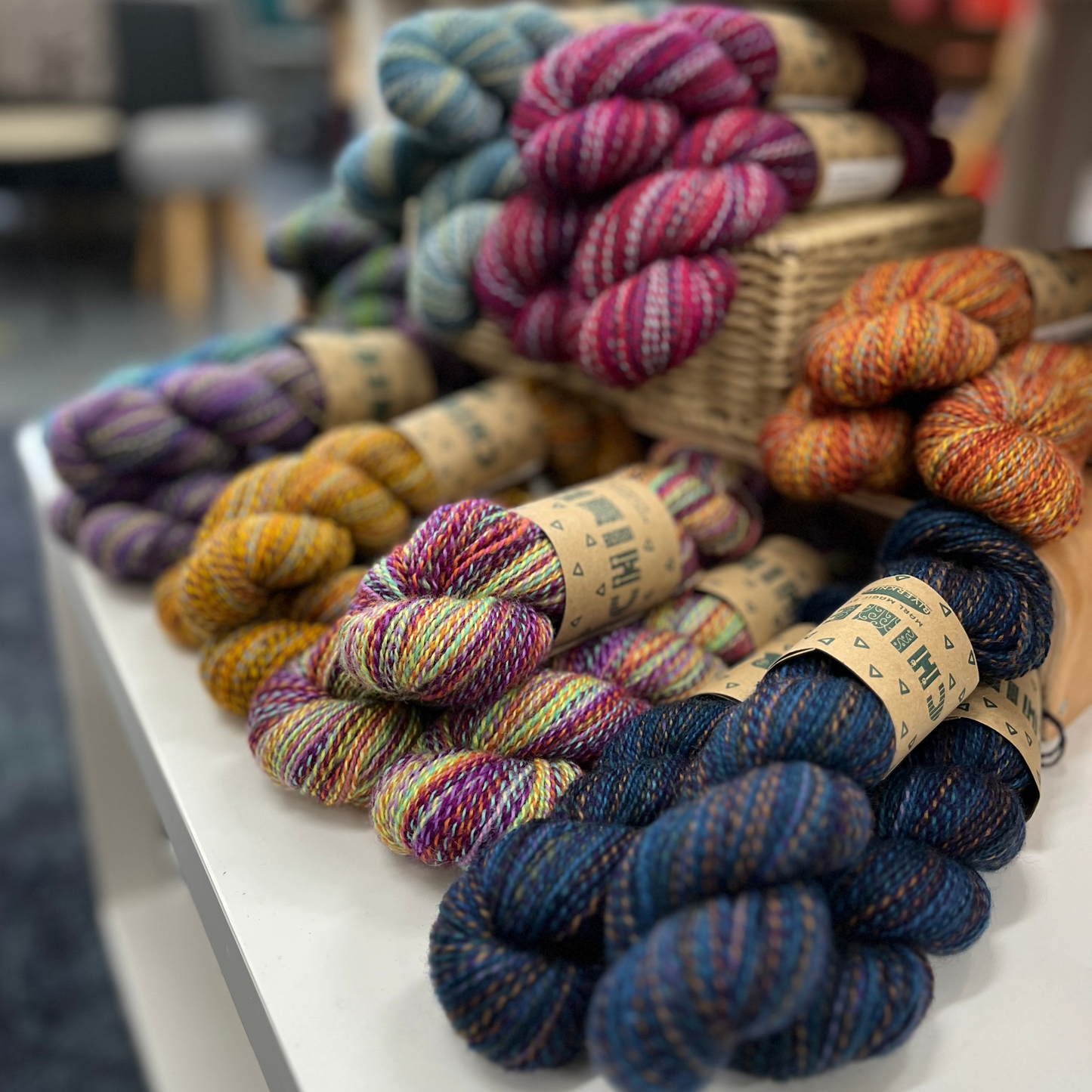 Chimera Yarn as it is on display in the shop; stacked in piles of 3 on a table.