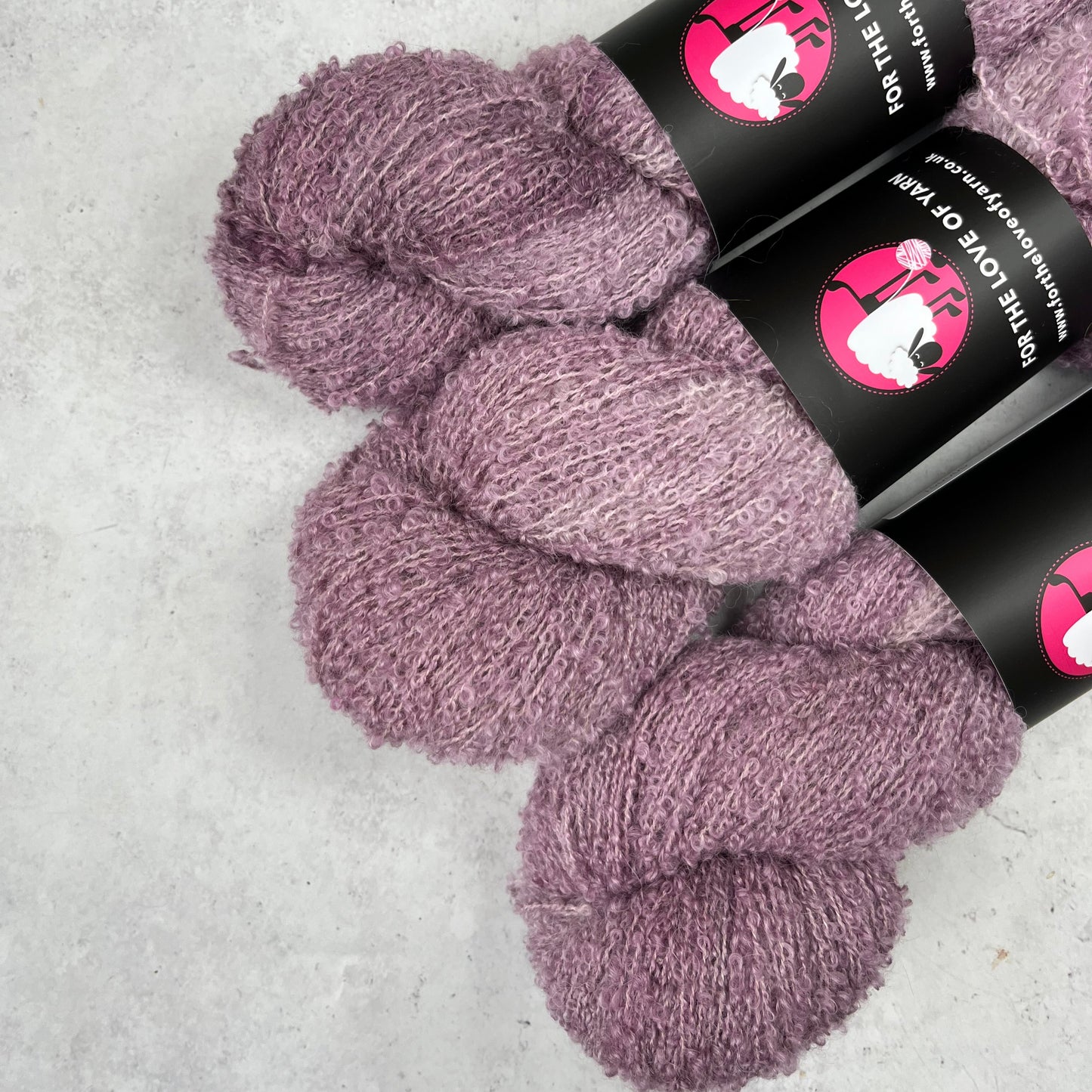 Three skeins of purple yarn with black labels on a light gray background