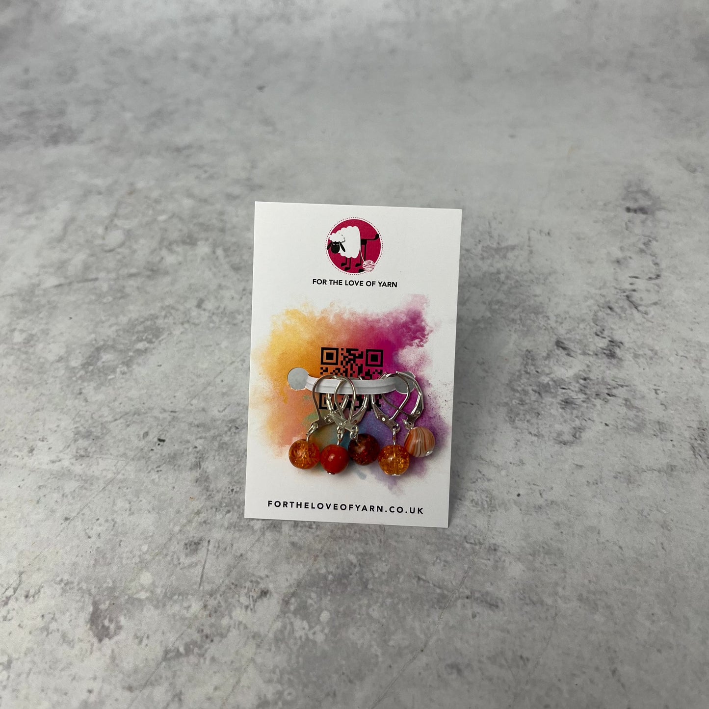 Set of orange crochet style stitch markers on backing card.