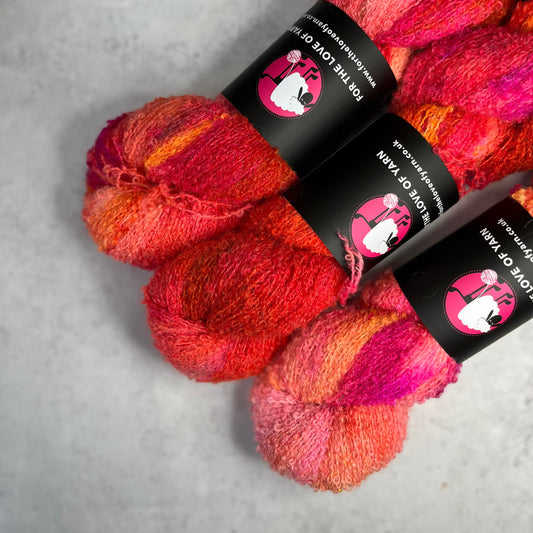 Three pink and red coloured skeins of yarn against a neutral background.