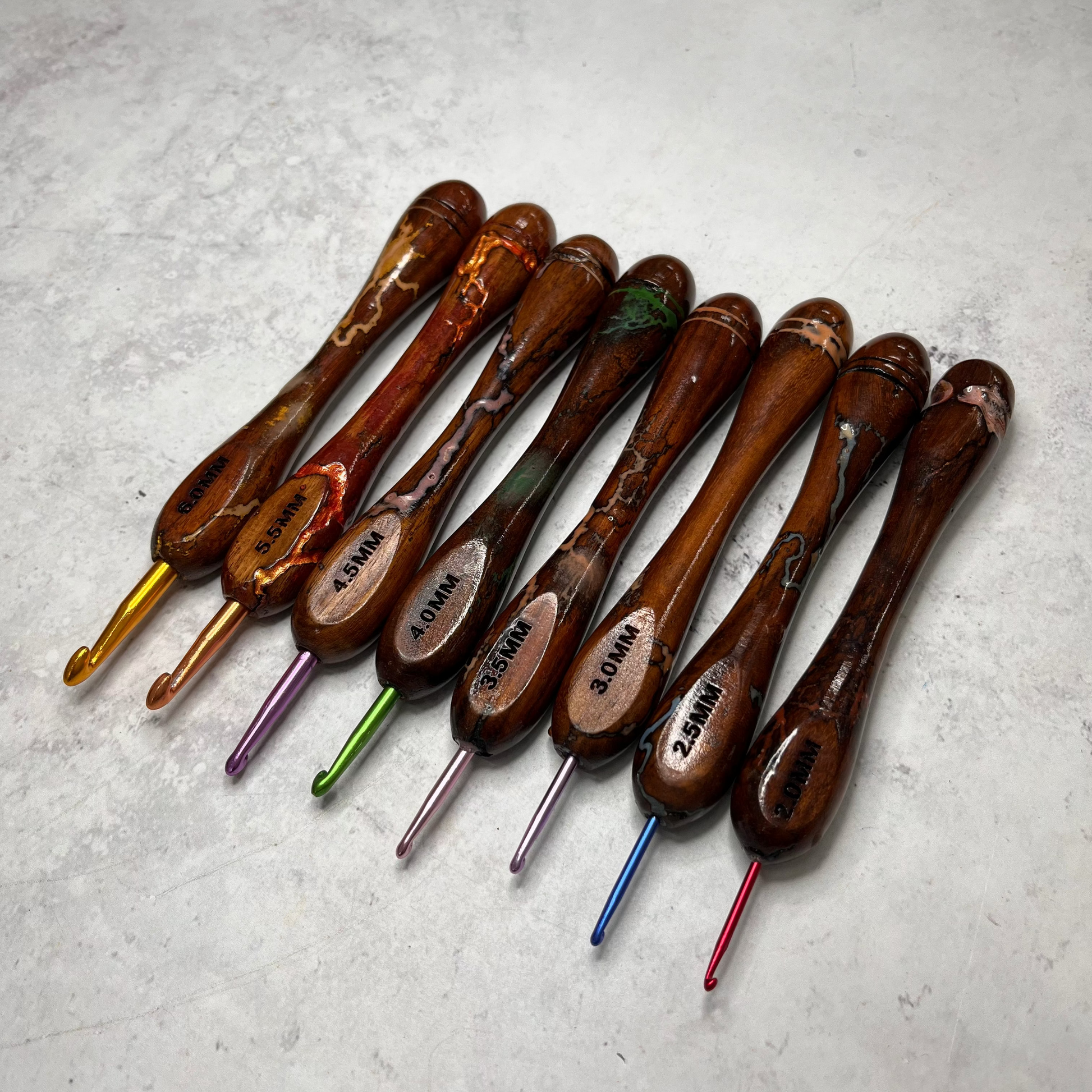 Wooden handled crochet hooks lined up in size order against a neutral background.