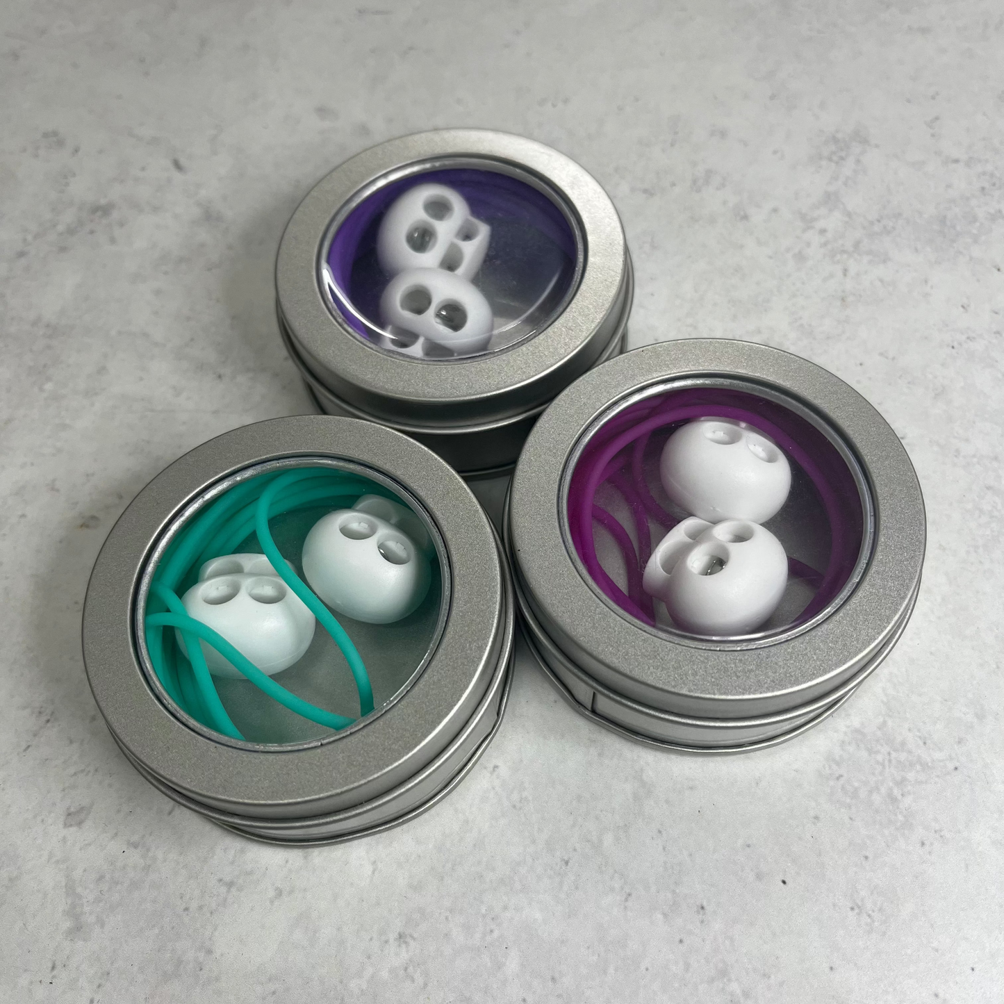 Three metallic containers with lids, each containing different items on a gray surface.