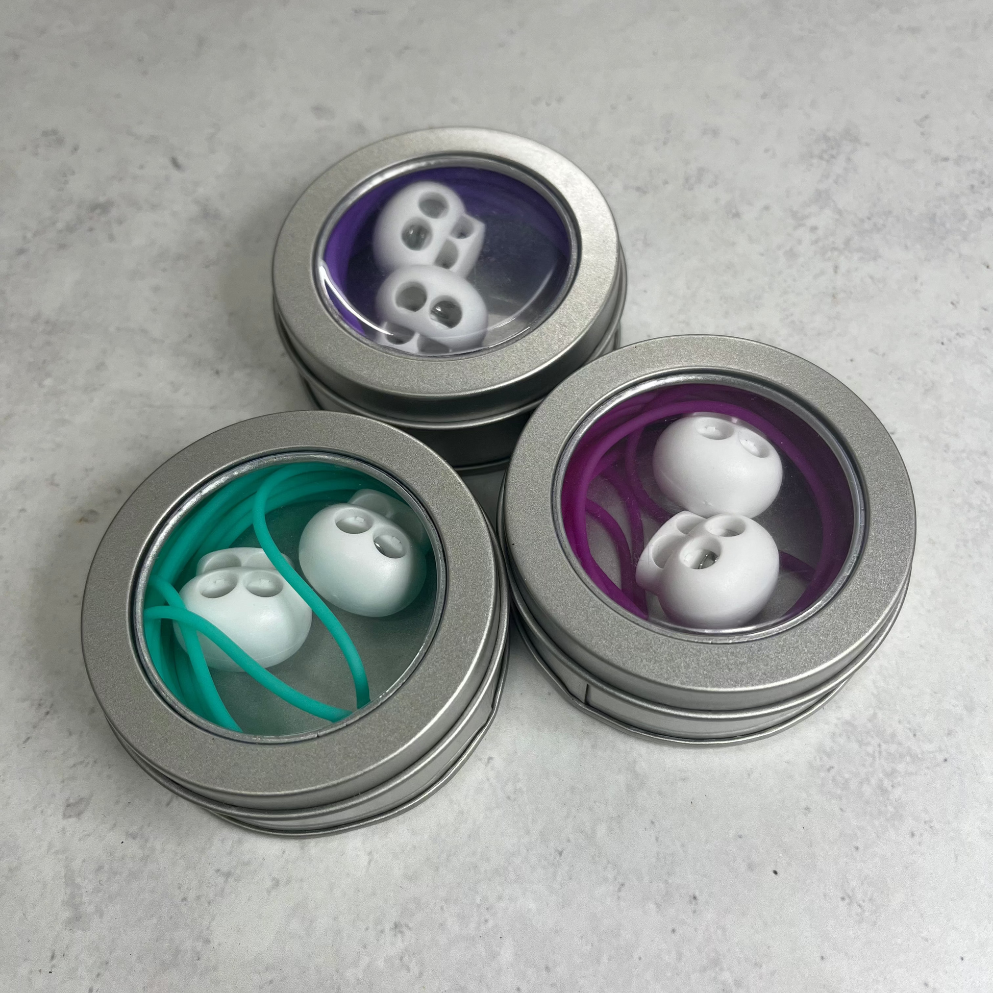 Three metallic containers with lids, each containing different items on a gray surface.