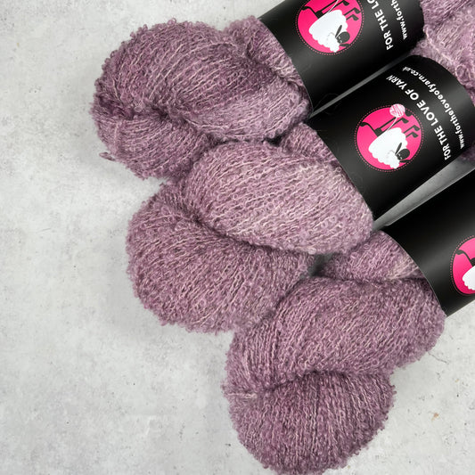 Three skeins of purple yarn with black labels on a light gray background