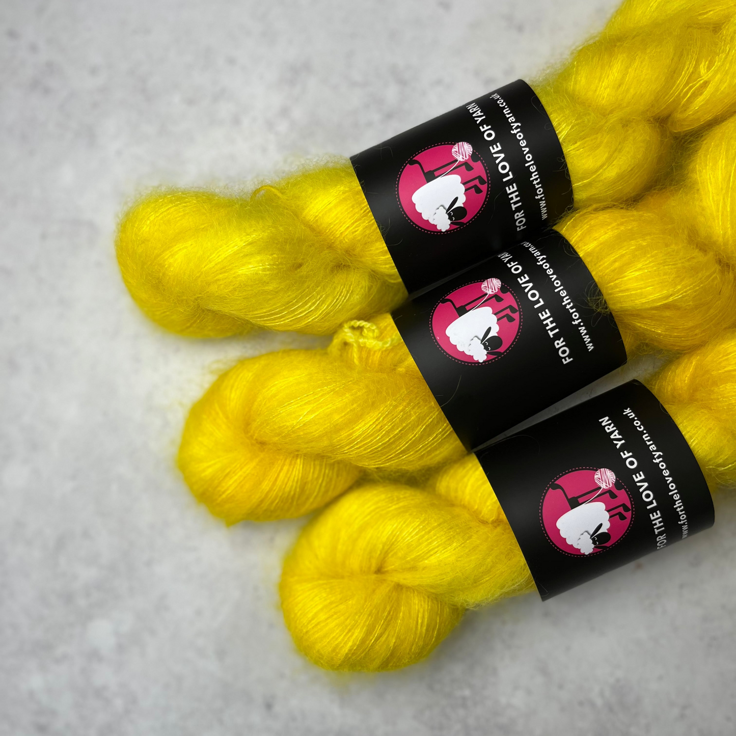 Three skeins of bright, zesty yellow mohair kid silk yarn laying side by side against a grey background.