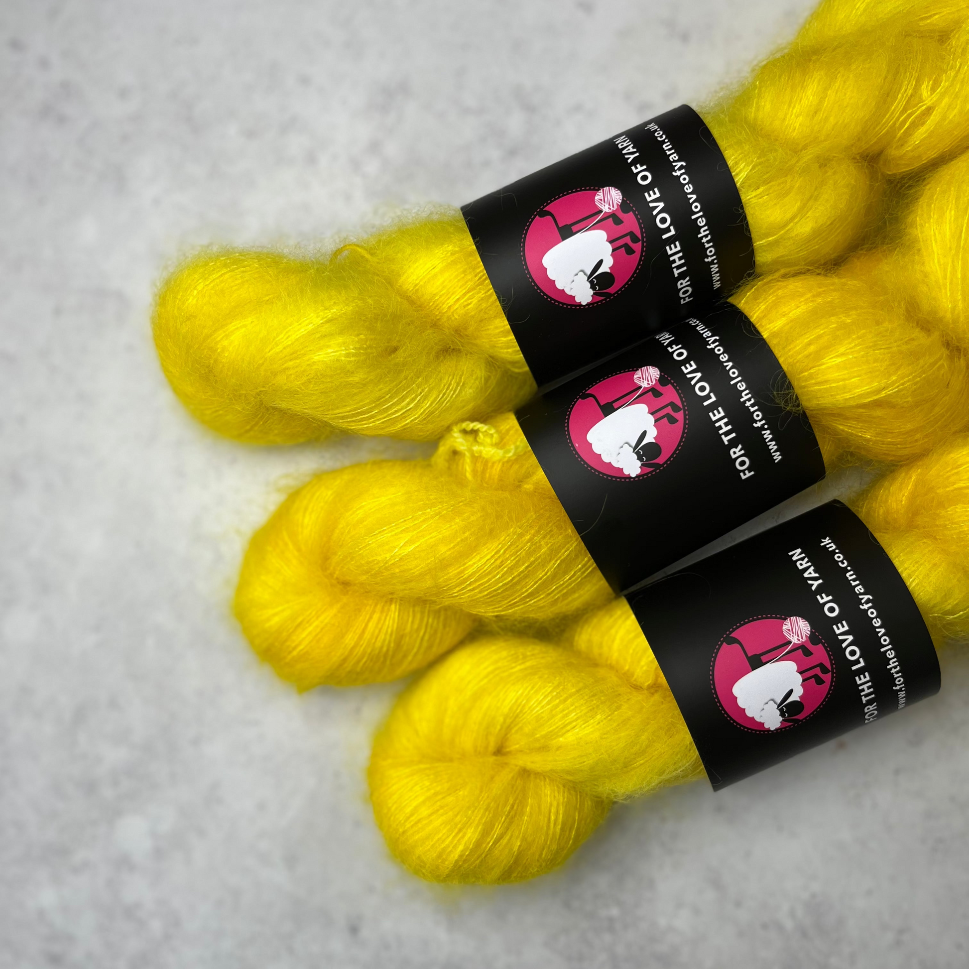 Three skeins of bright, zesty yellow mohair kid silk yarn laying side by side against a grey background.