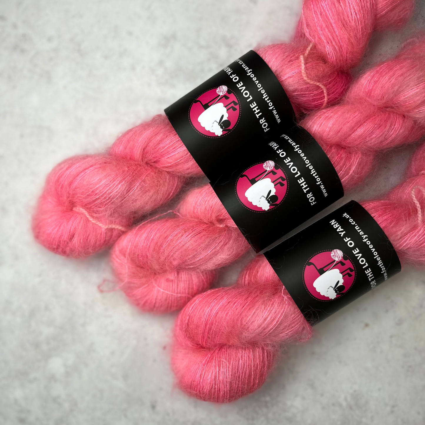 Three skeins of mohair silk yarn in a cool pastel pink, against a neutral grey background.