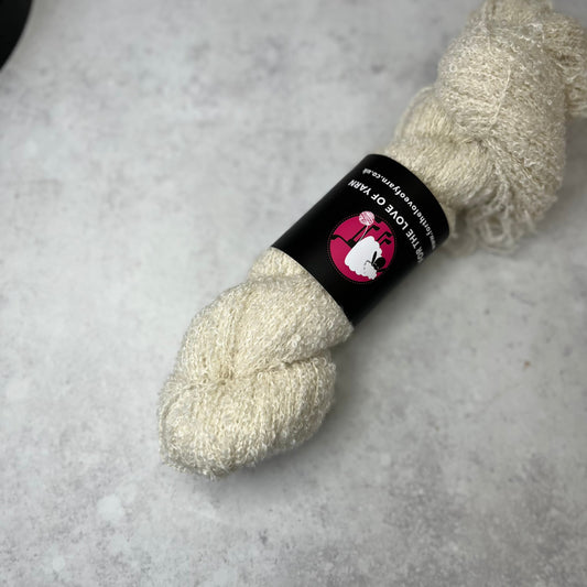 Skein of undyed baby silk boucle against a natural background.